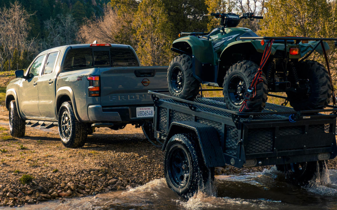 vue latérale arrière d'une Nissan Frontier 2023 qui remorque un VTT au travers un cours d'eau