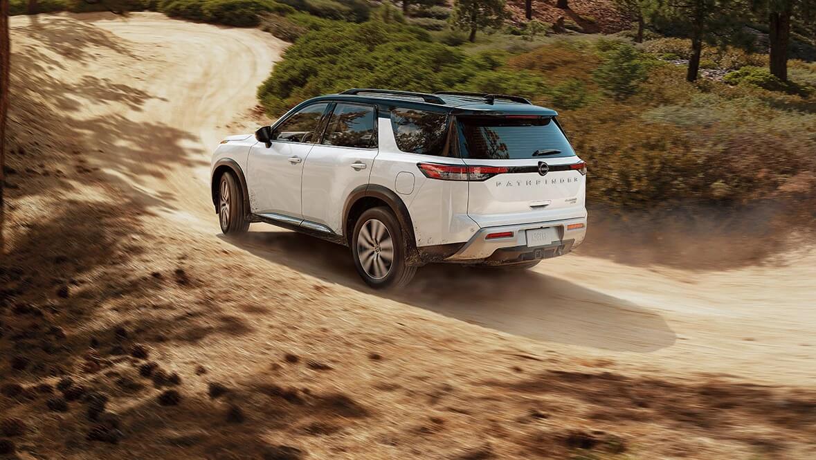 vue 3/4 arrière d'un Nissan Pathfinder 2022 Blanc et noir roulant sur un chemin de sable