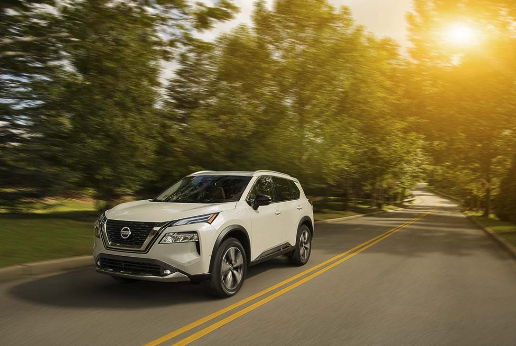 Nissan Rogue 2021 blanc roulant sur la route au bord des arbres