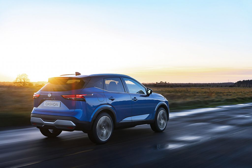 Vue arrière-latérale du Nissan Qashqai 2021 bleu roulant sur une longue route dans une campagne