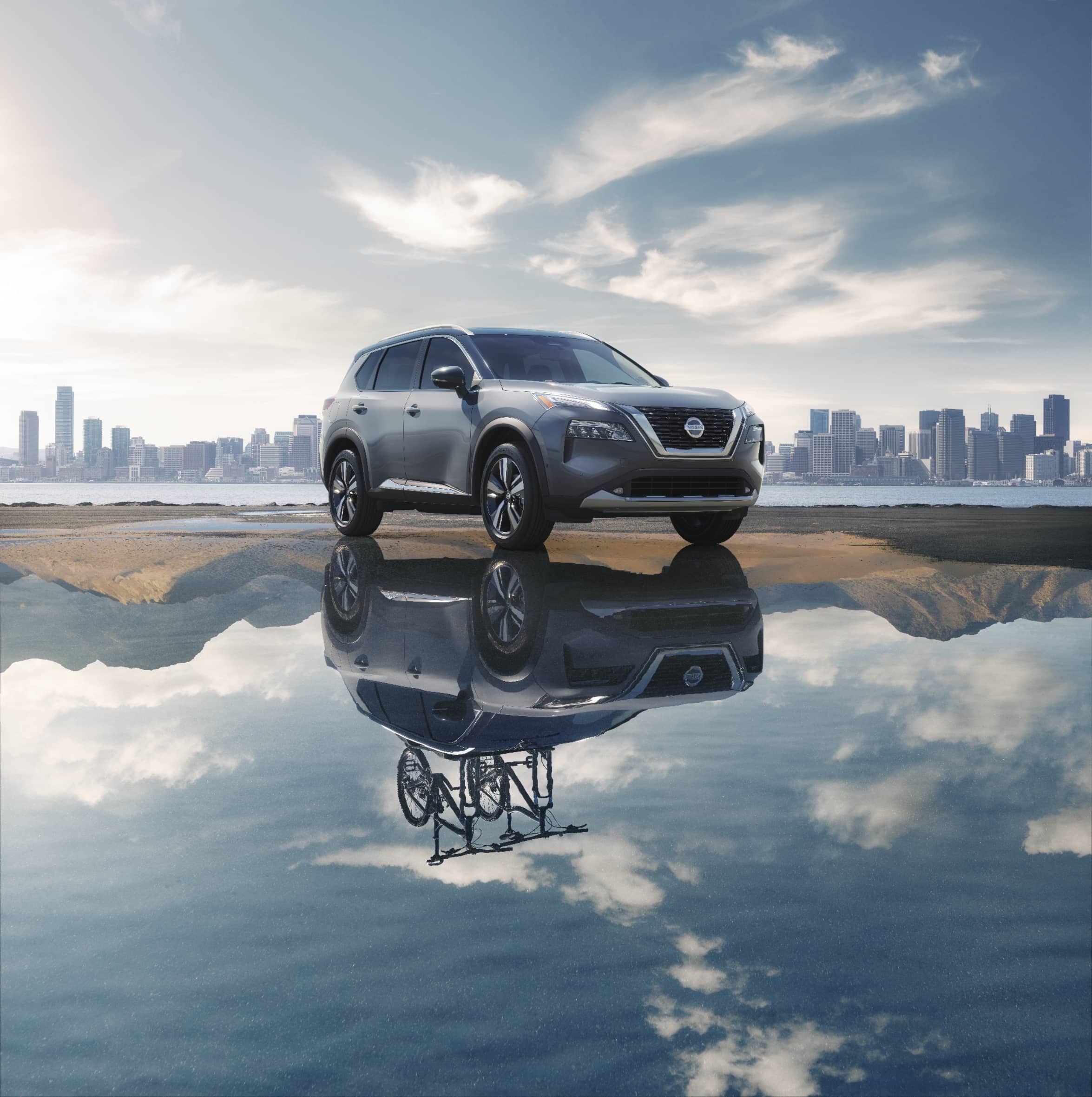 le tout nouveau Nissan Rogue 2021 gris sur un grand étang d'eau d'un fleuve avec une grande ville située au loin